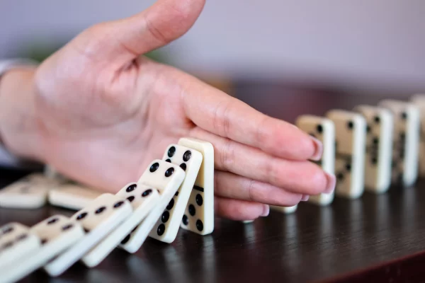 Hand stopping falling dominoes in a chain reaction, illustrating supply chain risk management, disruption prevention, business continuity, and operational resilience.