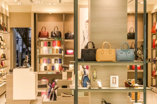 A brightly lit luxury boutique displays an array of handbags, colorful wallets, and stylish high heels on shelves, conveying elegance and sophistication.